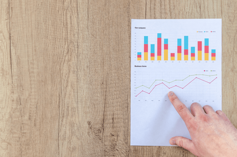 finger pointing to charts on paper placed on a wooden surface